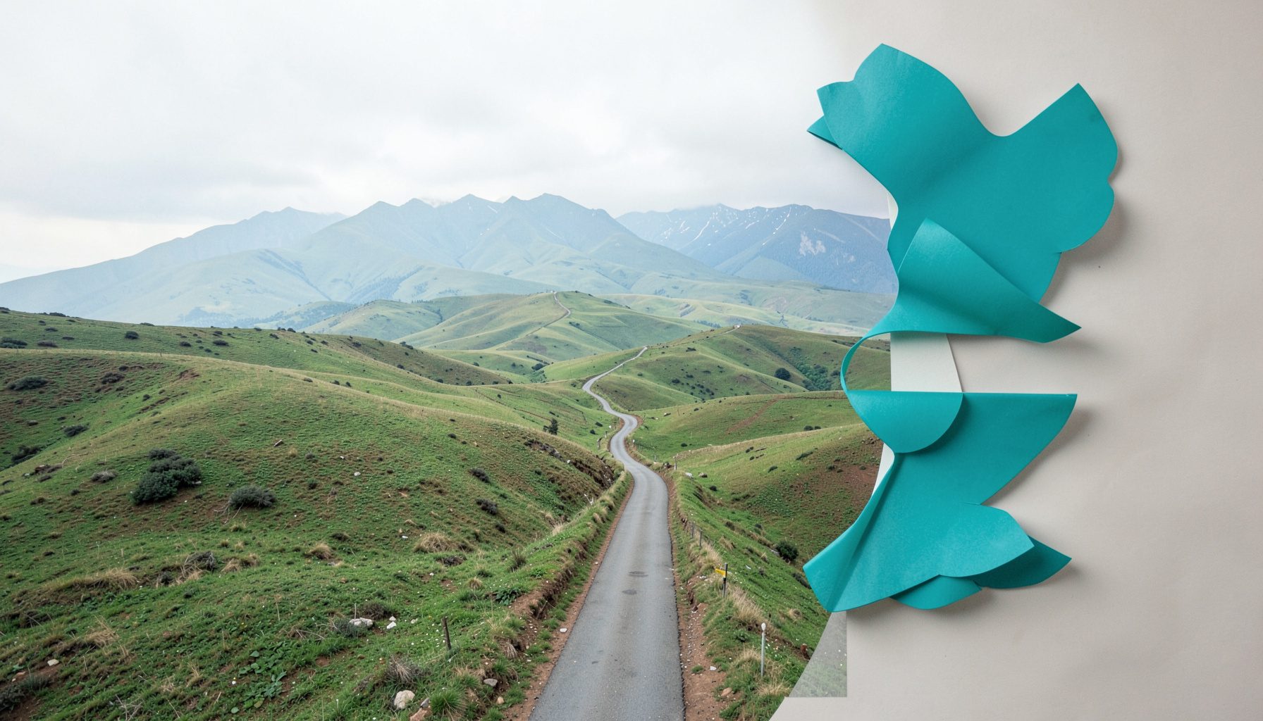 Wide landscape photograph of rolling green hills under a soft overcast sky, with a narrow winding road leading toward distant mountains. Muted greens, pale blues, and earthy browns dominate the scene, conveying calm and open space.